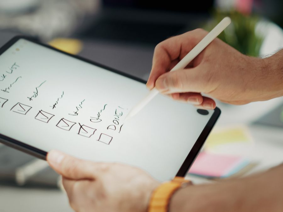 Close-up of a hand writing on a digital checklist using a stylus on a tablet, enhancing productivity.