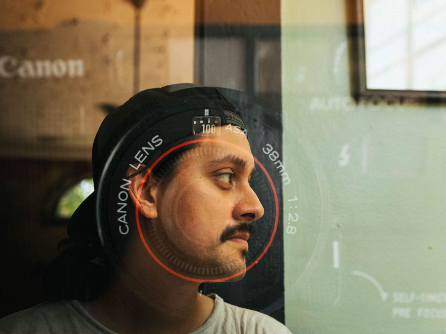 A creative portrait of a man behind glass with lens overlay reflection.