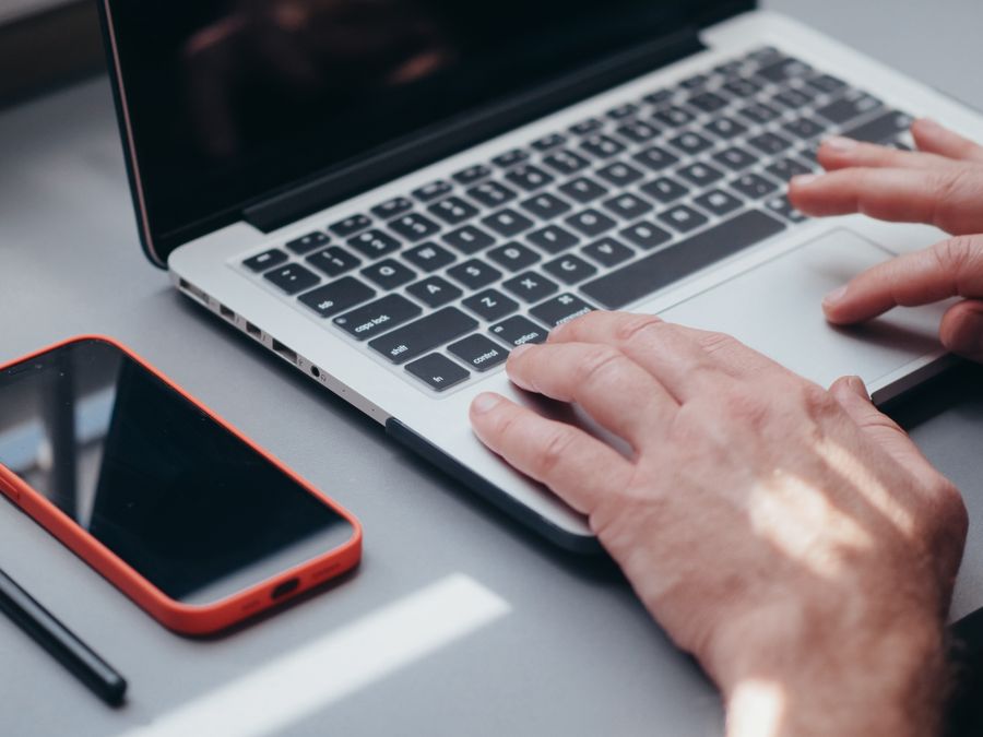 Hands typing on a laptop with a smartphone and pen on the side, perfect for tech and work themes.
