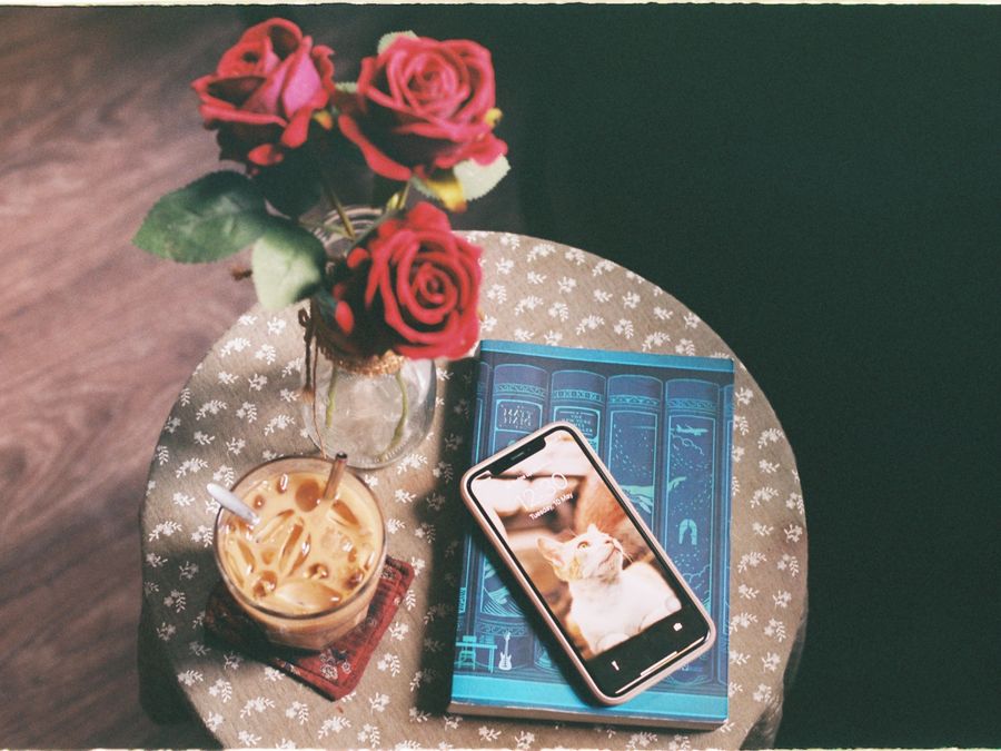 Aesthetic composition with roses, iced coffee, and smartphone on a vintage table.