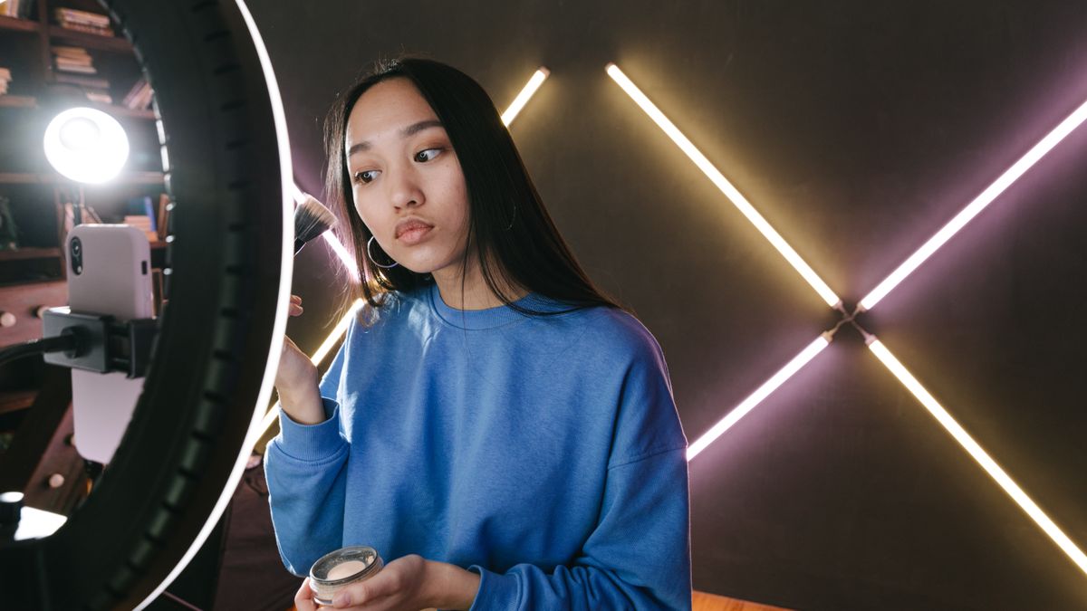 Woman applying makeup under ring light in modern indoor setting, perfect for beauty content creators.