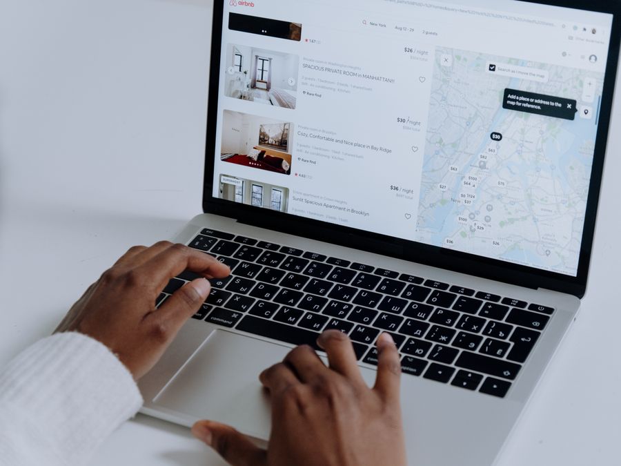 Hands typing on laptop searching Airbnb for accommodation options with map view.