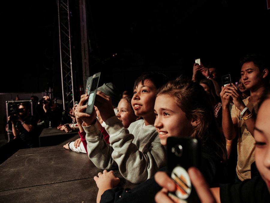 Kids capturing concert moments with smartphones at a lively event.