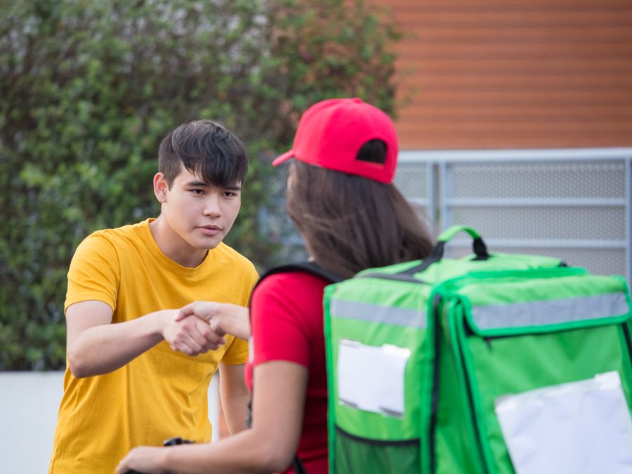 A delivery person in uniform shaking hands with a customer outdoors, representing delivery service.