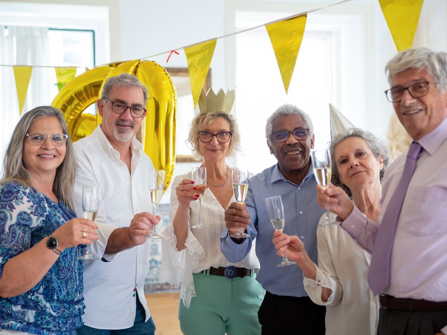 Elderly friends celebrating indoors with champagne, sharing smiles and joy at a festive party.