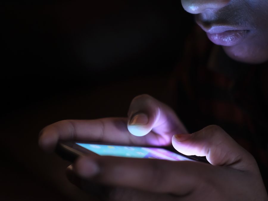 Close-up of a person holding and using an illuminated smartphone in a dark setting.