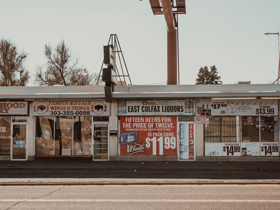 Vintage neighborhood liquor store and grocery with multiple signages on a sunny day.