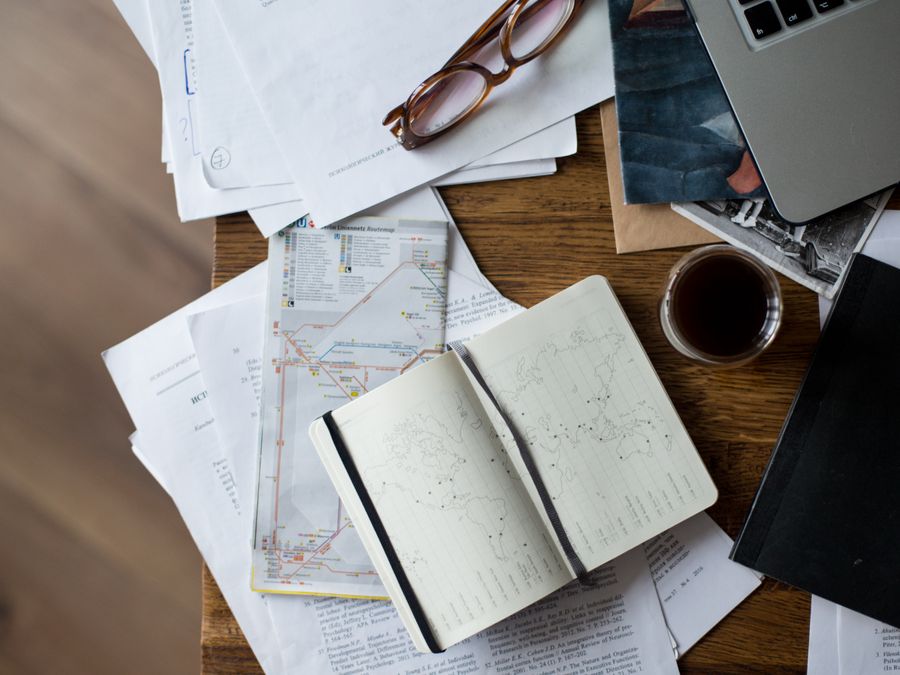 Flat lay of a workspace with coffee, maps, laptop, and documents on a wooden desk.