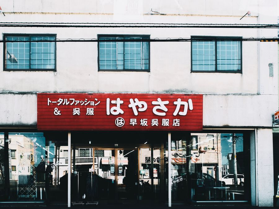 Street view of a Japanese clothing shop with a prominent red sign and glass windows.