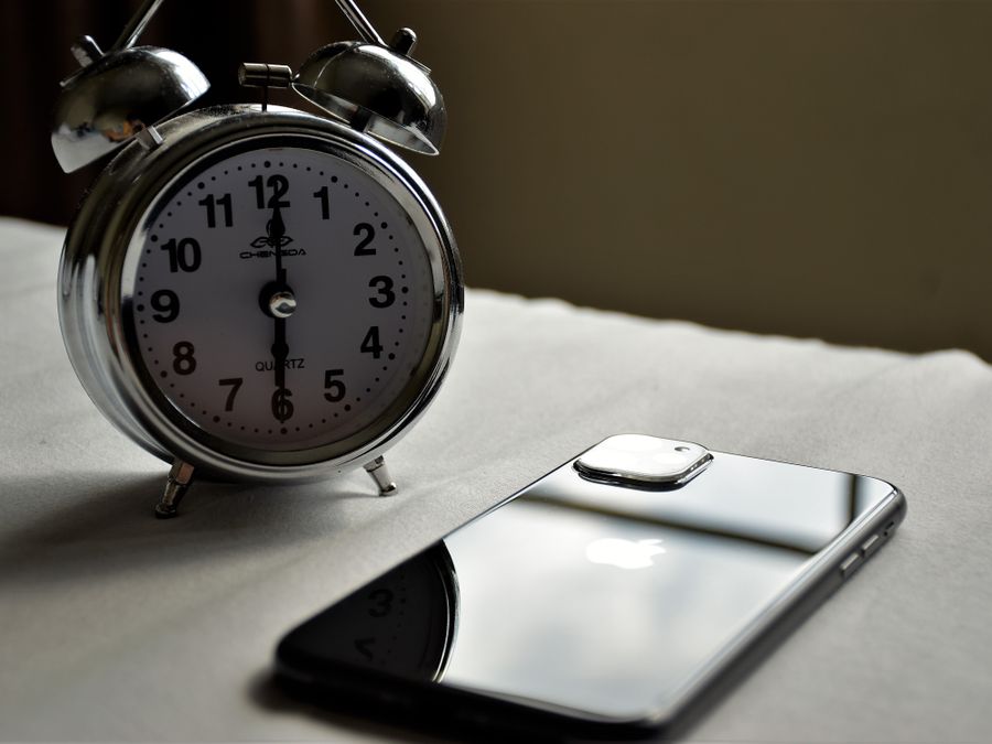 A classic silver alarm clock and modern smartphone placed side by side on a light surface.