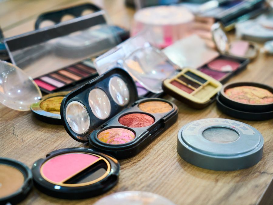 A variety of colorful makeup palettes and cosmetics organized on a wooden table.