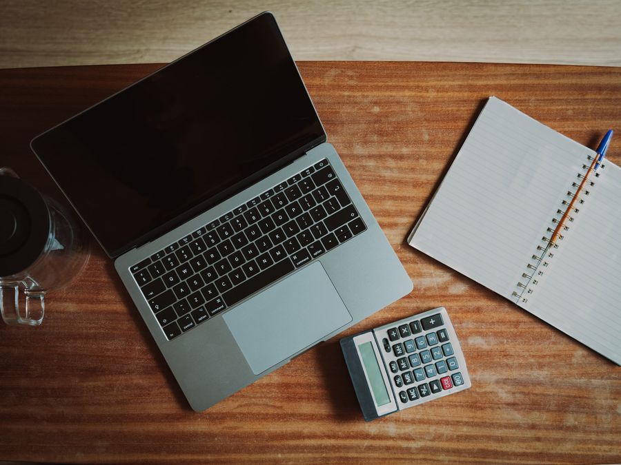 Top view of a desk with a laptop, calculator, and open notepad for work or study.