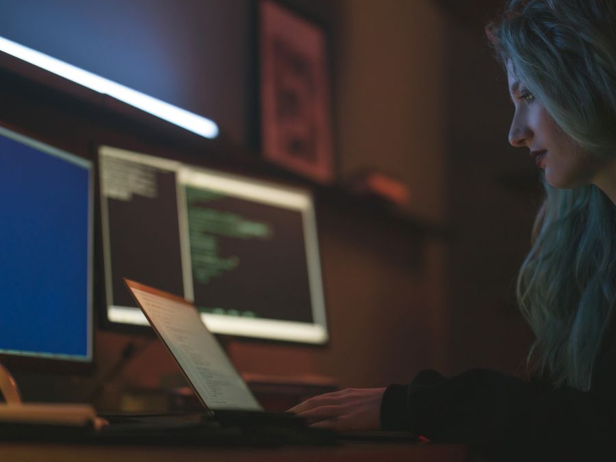 Woman working on cybersecurity programming with laptops and multiple screens
