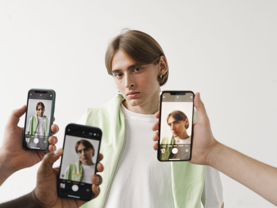 A man in a white shirt is being photographed with multiple smartphones against a plain background.