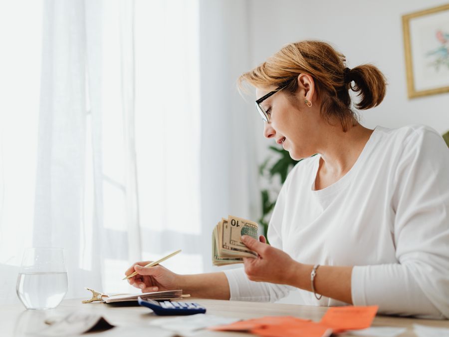 Businesswoman calculating finances with cash, calculator, and notebook at a bright desk.