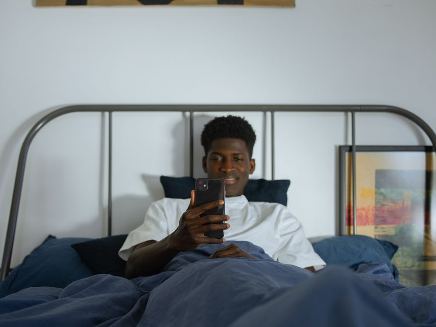 Young man using smartphone in bed, enjoying leisure time at home.