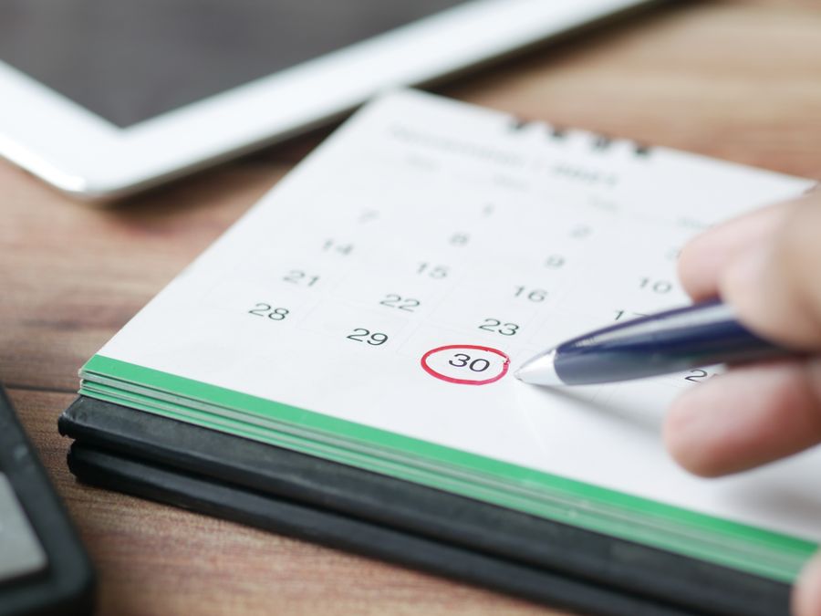 Close-up shot of a hand marking a date on a calendar with a pen, emphasizing planning and scheduling.