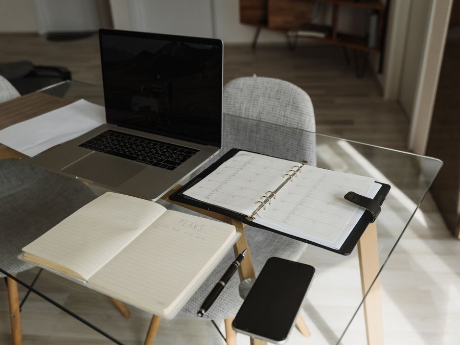 A clean and organized office setup with a laptop, notebook, and planner on a glass desk.