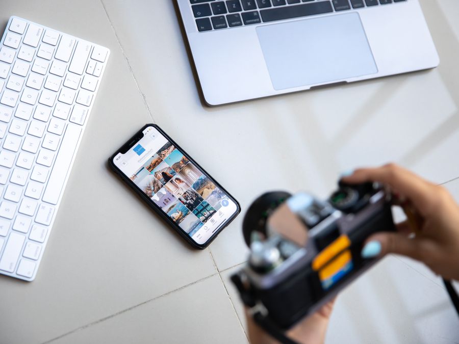 Person using vintage camera with smartphone and laptop in creative setup.
