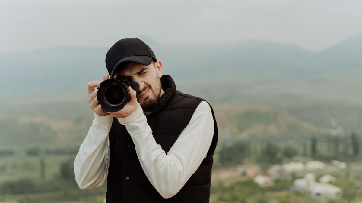 Male photographer holding a DSLR camera, capturing scenic views outdoors.