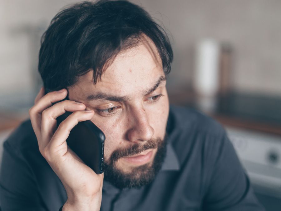 Thoughtful bearded man using smartphone, sitting indoors with a concerned expression.
