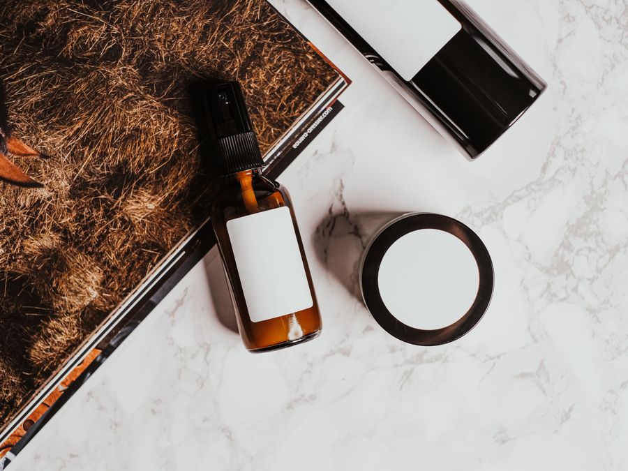 A stylish flatlay of skincare products with a magazine on a marble surface, ideal for product mockups.
