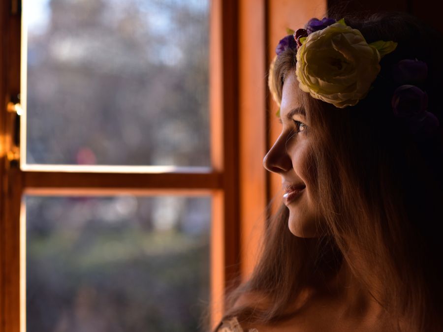 A serene profile portrait of a woman with a floral headband looking outside a window.