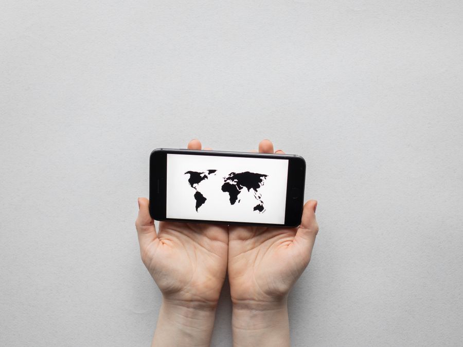 Hands holding a smartphone displaying a world map on a white background.