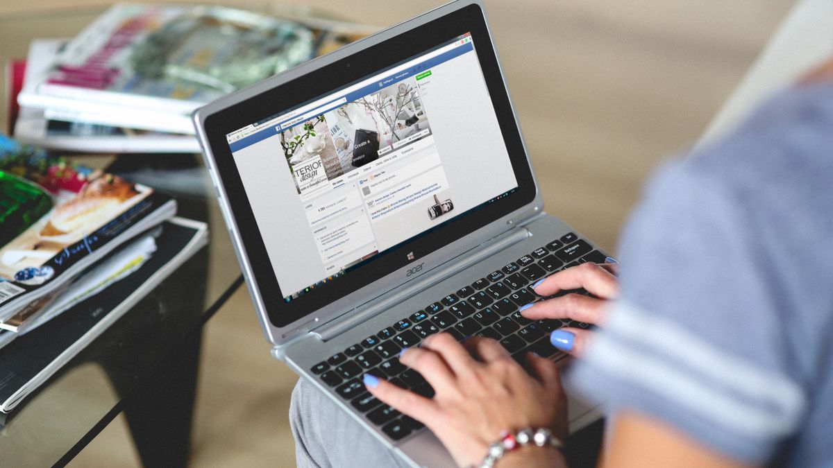 A woman typing on a laptop with social media on the screen, indoors setting.