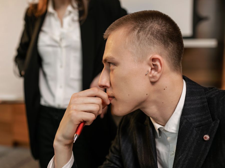 Side view of a thoughtful businessman holding a pen, contemplating in a modern office.