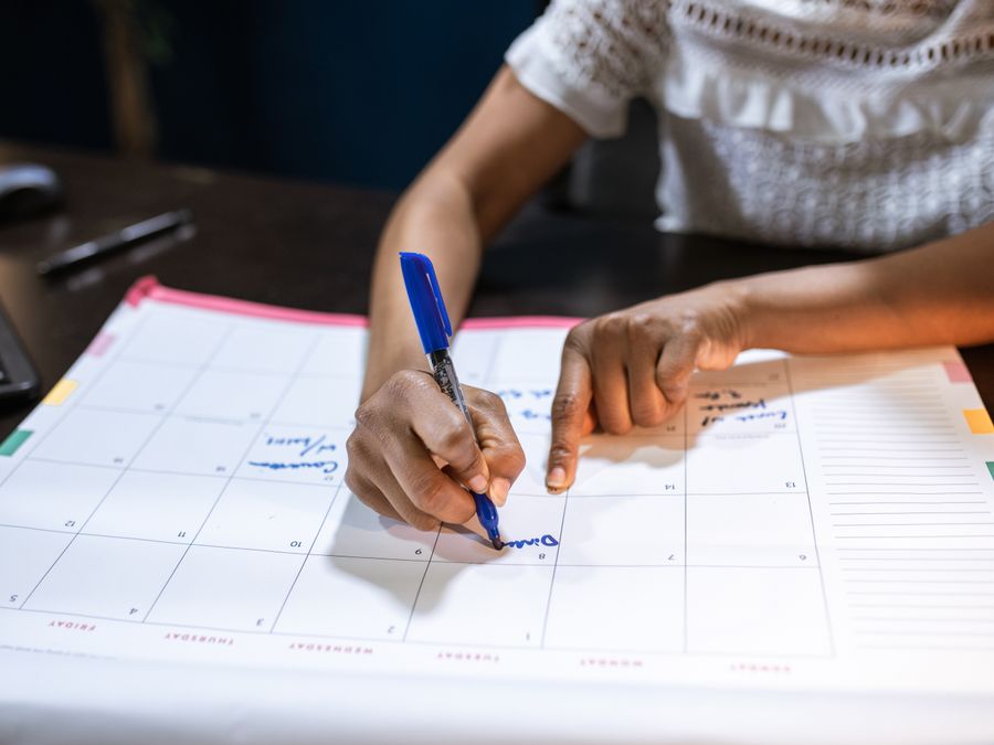 A woman marks important dates on her desk calendar, planning upcoming events.