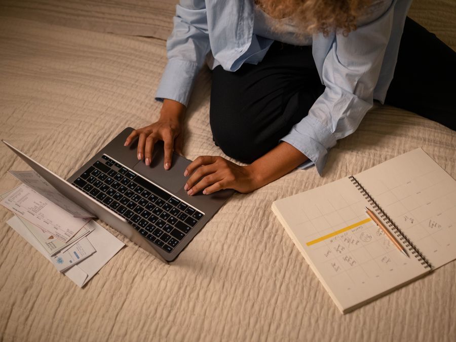 A woman working on a laptop while planning and organizing notes on a bed.