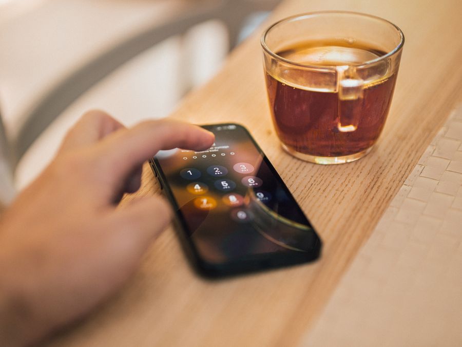 Close-up of hand unlocking a smartphone next to a cup of tea on a wooden table, emphasizing technology and security.