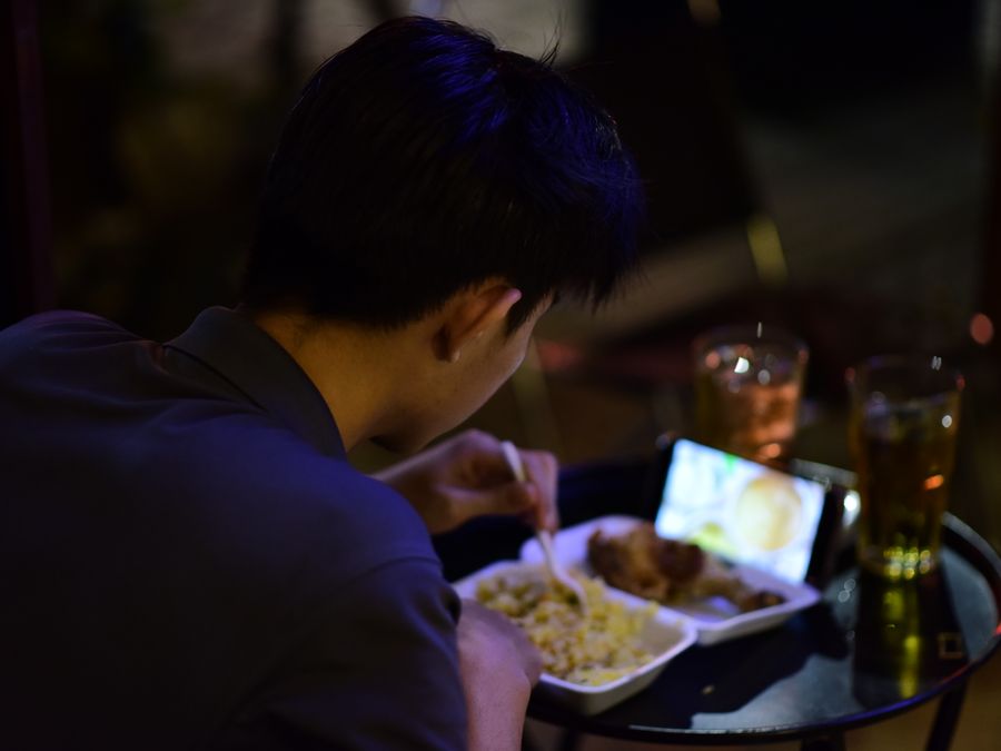 A young adult enjoys a meal while watching a video on their smartphone, creating a cozy night scene.