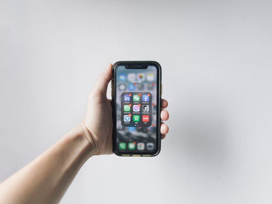 Hand holding smartphone displaying social media apps on home screen.