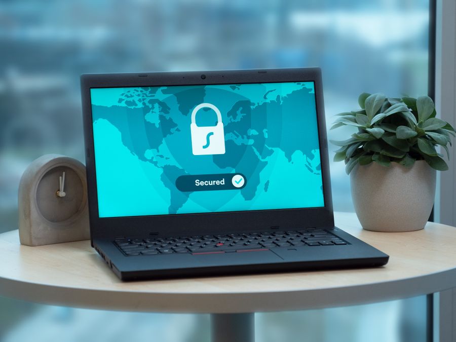 Laptop displaying a security lock icon on a table with a potted plant and clock.