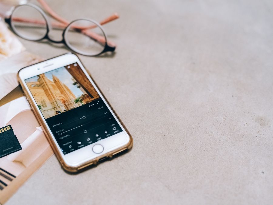 Smartphone displaying a photo editing app, next to a memory card and glasses on a table.