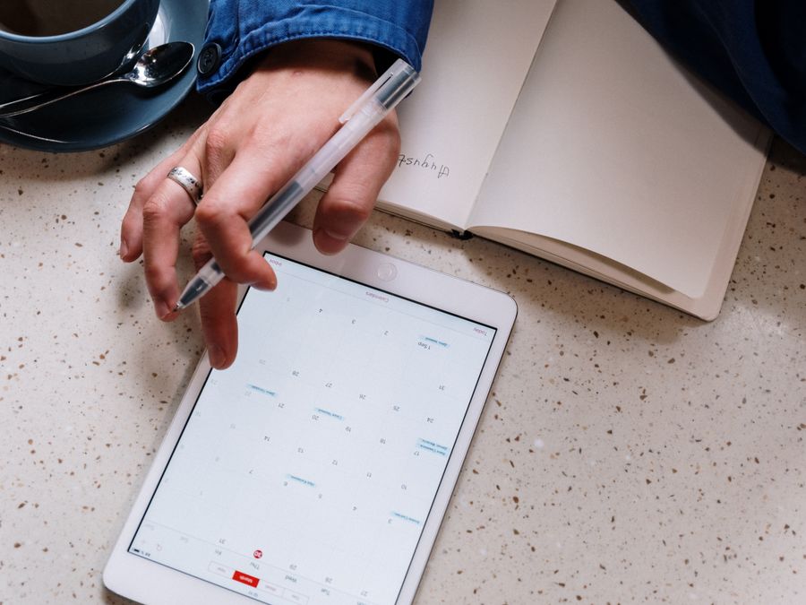 Person using a tablet for planning with an open notebook and coffee. Ideal for tech and productivity visuals.