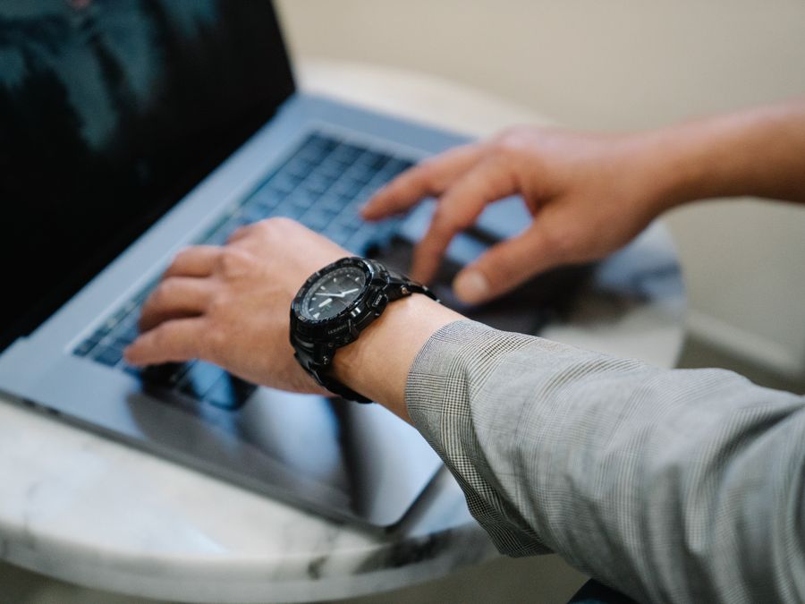 A person in business attire typing on a laptop, wearing a wristwatch, in a professional setting.
