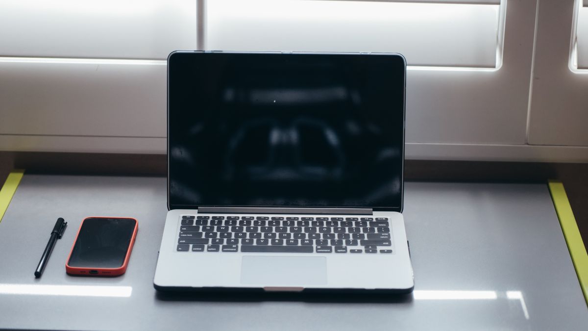 A minimalist desk setup featuring a laptop, smartphone, and pen under soft window light.