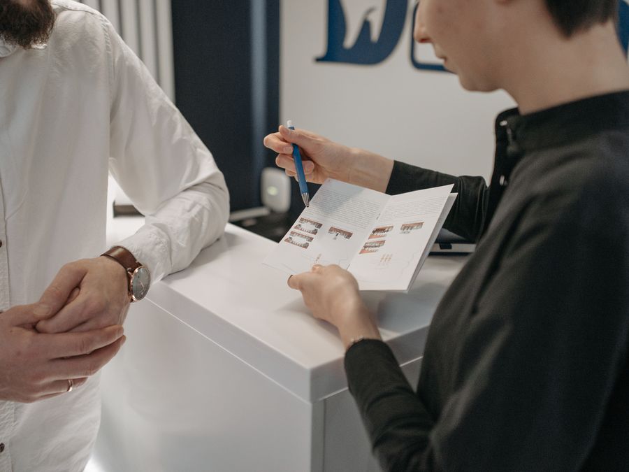Reception staff explaining information to a customer at a clinic counter.