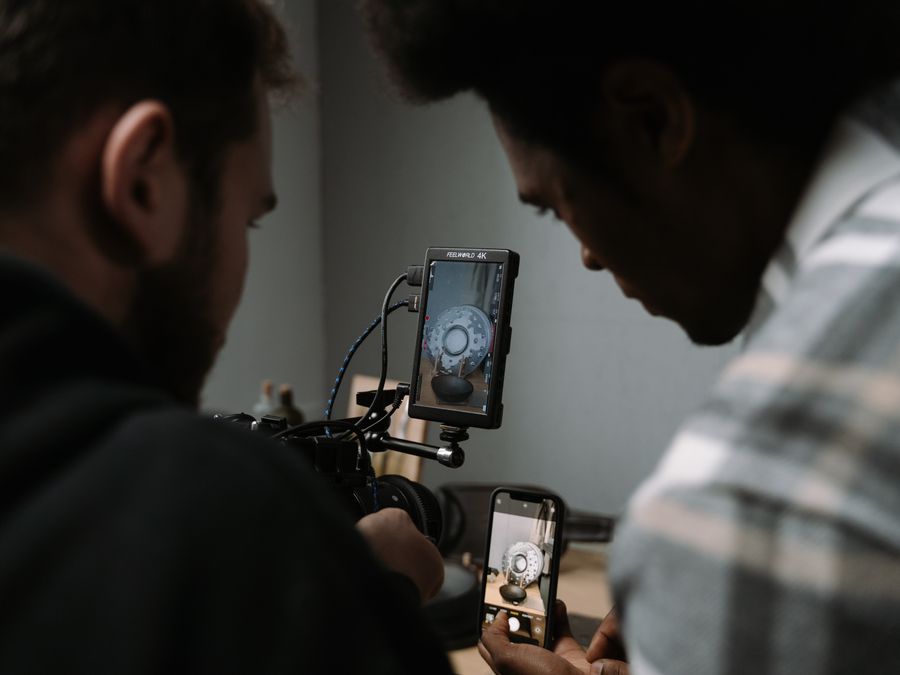 Two men use cameras and smartphones to capture a close-up video in a studio setting.