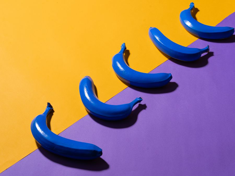 Creative arrangement of blue bananas on a vibrant yellow and purple backdrop.