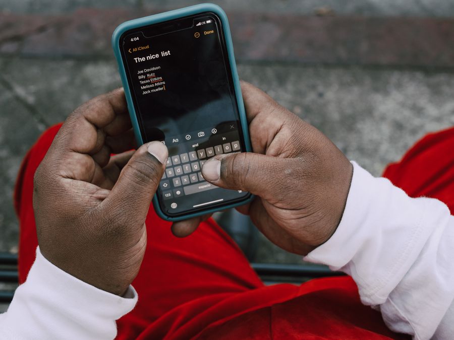 A person typing on a smartphone outdoors, wearing a red and white outfit, capturing a close-up view.
