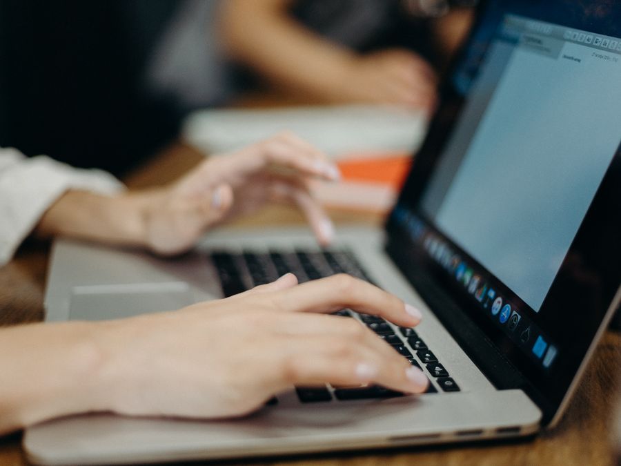 Person typing on a laptop in an office setting. Focus on hands and keyboard.