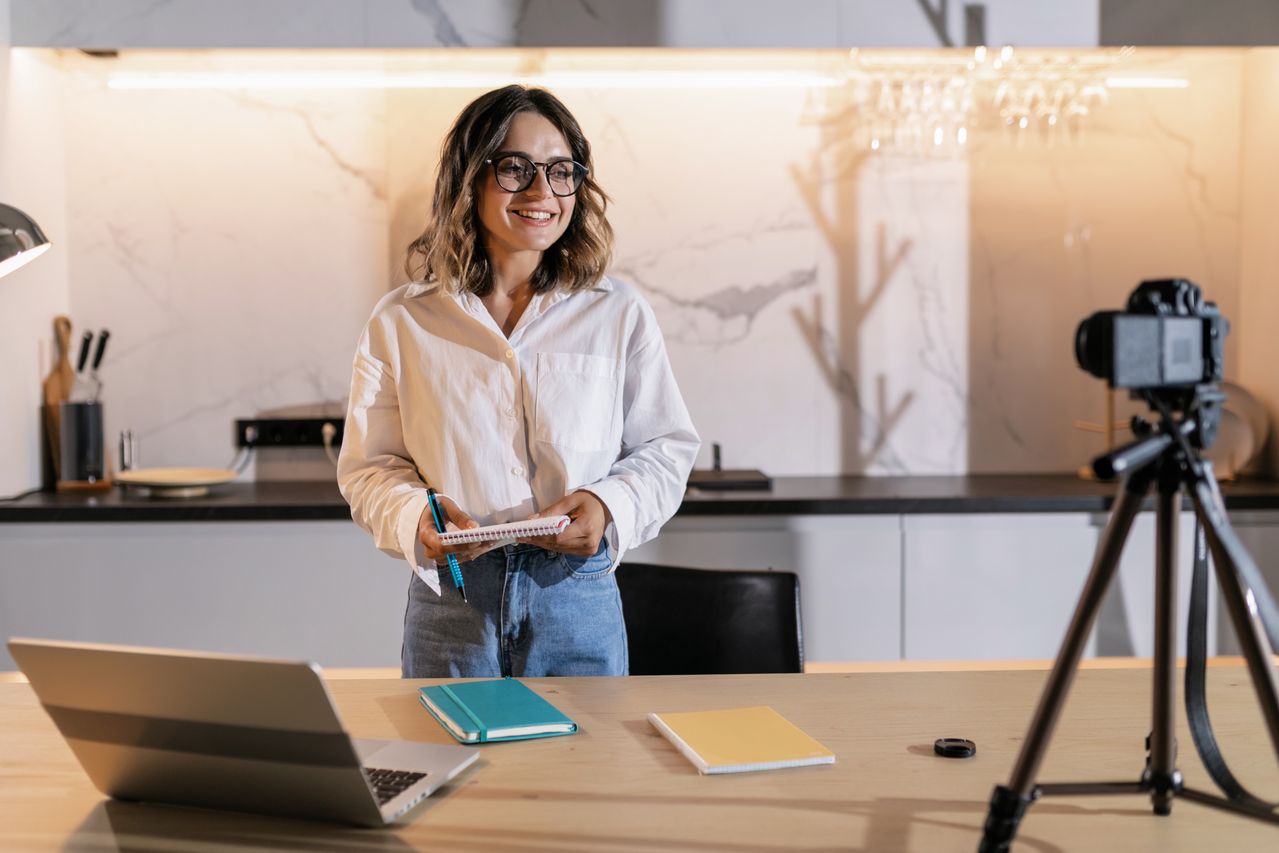 Influencer recording social media content with a camera, laptop, and planning notes in a professional home workspace