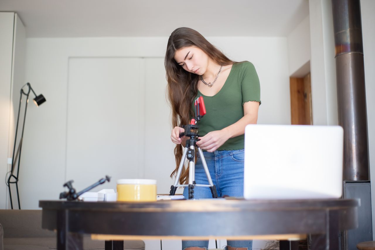 Content creator setting up filming equipment in a home workspace while managing an independent social media business