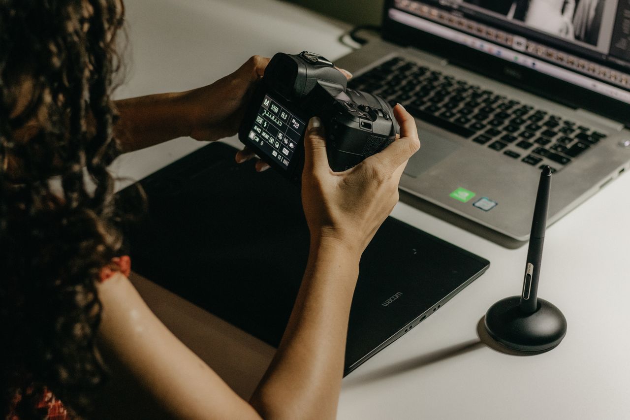 Content creator managing camera files and visual media on a laptop for social media campaign production and archiving